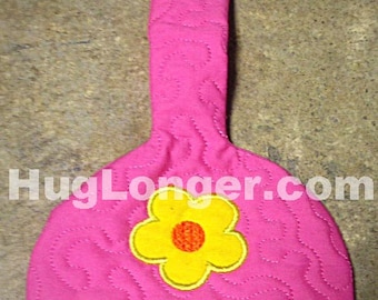 May include: Pink quilted kitchen towel holder with a yellow flower design and a pink fabric loop with an orange button. HugLonger.com is printed on the holder.