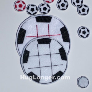 Può includere: Due palloni da calcio in feltro bianco con cuciture nere. Il pallone più grande ha una linea rossa cucita al centro. Il pallone più piccolo ha un motivo a griglia di cuciture nere. HugLonger.com è stampato sotto i palloni.