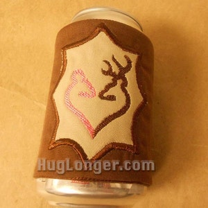 May include: A brown can cooler with a tan emblem featuring a pink heart and a brown deer antler design. The cooler has the text "HugLonger.com" at the bottom. The cooler is wrapped around a silver can.