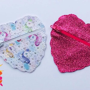 May include: Two heart-shaped zipper pouches. One pouch is pink glitter fabric and the other is white fabric with a unicorn print. Both pouches have a zipper closure.
