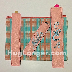 May include: Three pink fabric pouches with different embroidery. The pouches are on a plaid fabric background. The pouches are labeled "Nails", "C & A" and one is blank.