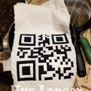 Puede incluir: Una toalla de cocina blanca con un código QR en blanco y negro impreso en ella. El texto "Hug Longer" está impreso debajo del código QR.