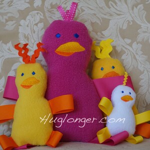 May include: Three plush toy birds, one pink, one yellow, and one white. The pink bird is the largest and has a white polka dot bow on its head. The yellow bird has orange curly hair and orange ribbon wings. The white bird has yellow ribbon wings. The birds are all sitting on a beige fabric background. Huglonger.com is printed on the fabric.