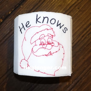May include: White toilet paper roll with a red embroidered Santa Claus face and the text "He knows" in black.