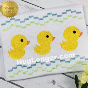 May include: A digital embroidery design featuring three yellow rubber duckies with black eyes and orange beaks. The ducks are arranged in a row and are surrounded by a blue and green zig-zag pattern.