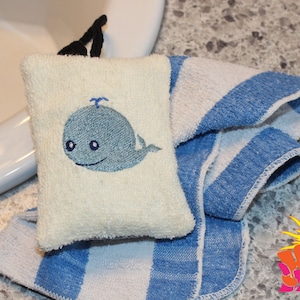 May include: A white washcloth with a blue whale embroidered on it. The washcloth is folded and placed on top of a blue and white striped towel.