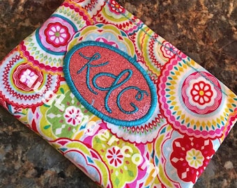 May include: A small, colorful fabric pouch with a pink and turquoise monogram "K&G" embroidered on the front. The pouch has a paisley pattern with red, pink, yellow, blue, and green colors.