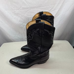 K&ouml;nnte beinhalten: Ein Paar schwarze Cowboystiefel aus Leder mit spitzer Zehenpartie, einem Blockabsatz und dekorativen grauen Ziern&auml;hten am Schaft. Die Stiefel verf&uuml;gen &uuml;ber Anziehschlaufen am oberen Rand und ein beiges Innenfutter in klassischer Western-Optik.