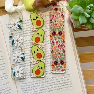 May include: A set of three ceramic mugs with a speckled, cream-colored glaze. Each mug features a different hand-painted design: a blue and green leaf, a yellow flower, and a red berry. The mugs have a capacity of approximately 12 ounces.