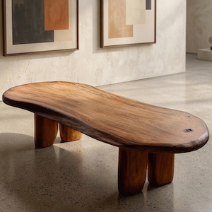 Puede incluir: Banco de madera maciza con borde natural y tres pares de patas redondeadas. El banco es de color marrón cálido y tiene una superficie lisa y pulida. El diseño es moderno y minimalista.