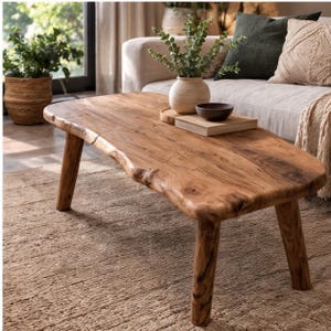 Pode incluir: Uma mesa de centro baixa feita de madeira natural castanho-clara com acabamento de borda viva e quatro pernas cilíndricas robustas. A superfície exibe um padrão de grão de madeira proeminente, destacando a textura orgânica e tons quentes.