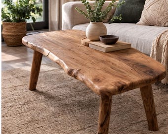 May include: A low coffee table crafted from natural light brown wood with a live edge finish and four sturdy, cylindrical legs. The surface displays a prominent wood grain pattern, showcasing the organic texture and warm tones of the timber.