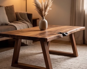 May include: A solid wood coffee table with a natural edge and a warm brown finish. The table has a rectangular top and angled legs. A white vase with dried ornamental grass sits on the table. The table measures approximately 48 inches long.