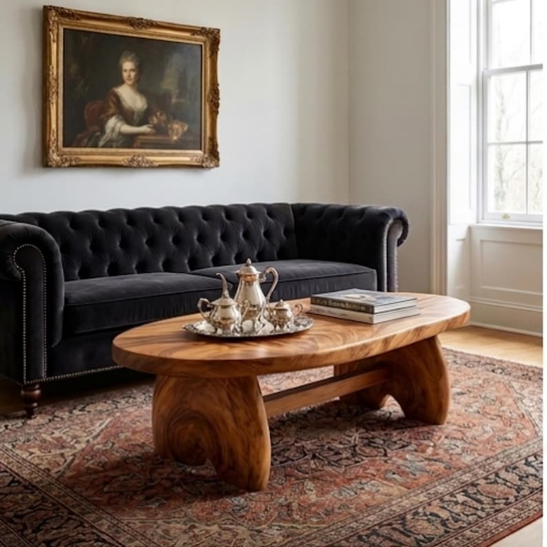 K&ouml;nnte beinhalten: Ein niedriger, ovaler Couchtisch aus naturfarbenem, hellbraunem Holz mit einer dicken, glatten Tischplatte und zwei stabilen, geschwungenen Sockelbeinen. Der Tisch zeigt eine sichtbare Holzmaserung und steht vor einem dunkelgrauen Polstersofa.