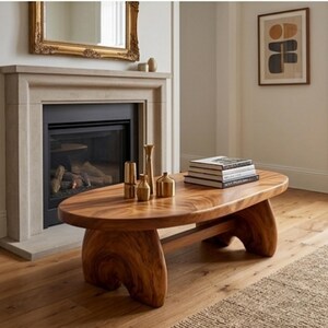 K&ouml;nnte beinhalten: Ein ovaler Couchtisch aus Holz mit nat&uuml;rlicher Maserung und zwei geschwungenen Beinen aus Massivholz. Auf der Tischoberfl&auml;che stehen drei kleine, goldfarbene Metallvasen in unterschiedlichen H&ouml;hen sowie ein Stapel aus vier gebundenen B&uuml;chern.