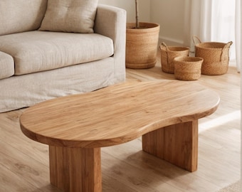 May include: A low coffee table crafted from light brown wood with a smooth, organic, kidney-bean-shaped top and two sturdy, rectangular slab legs. The surface displays a natural wood grain pattern, providing a clean and functional furniture piece.