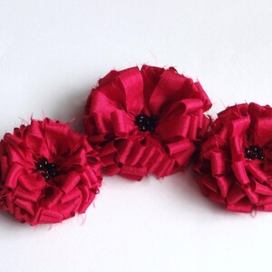 May include: Three red fabric flowers with black centres. The flowers are arranged in a row, with the centre flower slightly higher than the other two.