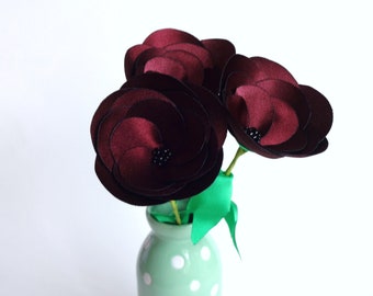May include: Three dark red fabric flowers with black centers in a green and white polka dot vase.