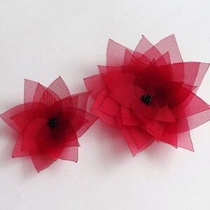 Peut inclure: Deux fleurs en tissu rouge avec des centres noirs. La plus grande fleur est à droite et la plus petite fleur est à gauche.