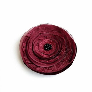 May include: A burgundy fabric flower brooch with a black bead center.