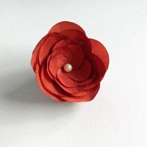 May include: A red paper flower with a white pearl in the center.