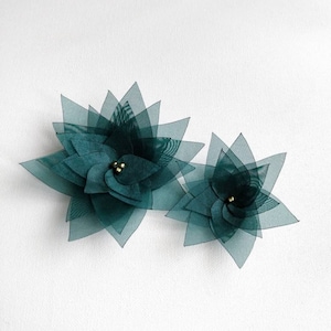 May include: Two teal green fabric flowers with gold centers. The flowers are layered and have a delicate, airy appearance.