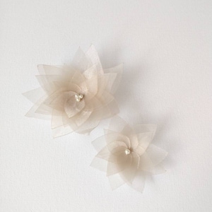 May include: Two beige fabric flowers with pearl centers. The larger flower is in the background and the smaller flower is in the foreground.