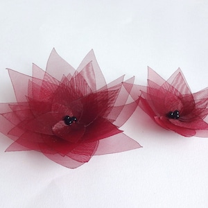 May include: Two burgundy fabric flowers with black bead centers. The larger flower is about 5 inches in diameter and the smaller flower is about 3 inches in diameter.
