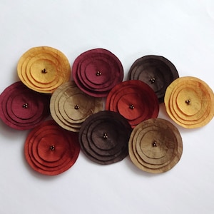 May include: Assortment of handmade paper flowers in shades of burgundy, brown, and gold. Each flower is layered and has a small bead in the center.