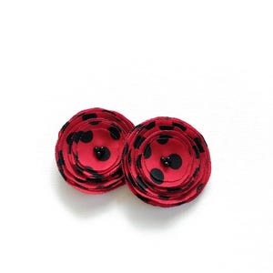 May include: Two red fabric flower-shaped hair accessories with black polka dots and a black bead center. The layered petals create a dimensional effect. These accessories are suitable for various hairstyles.