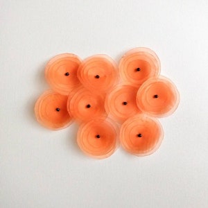May include: A cluster of ten peach-colored fabric flowers with black centers. The flowers are arranged in a loose, organic pattern.