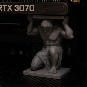 May include: A gray statue of Atlas kneeling and supporting a black RTX 3070 graphics card. The statue is on a gray base. The graphics card has the text "RTX 3070" in white.