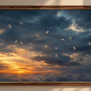 May include: A rectangular wall art print in a dark wood frame featuring a sunset sky filled with dark blue and orange clouds. A flock of small white birds is flying across the horizon above a dense layer of clouds illuminated by the sun.