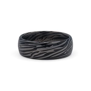 Pode incluir: Um anel cinza escuro com um padrão de listras de zebra. O anel é do estilo banda, com uma forma arredondada. O anel é feito de um material sólido e está sobre um fundo branco.