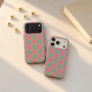 May include: Two rectangular smartphone cases featuring a repeating checkered pattern in alternating shades of bright pink and light green. Each case has a dedicated cutout for a triple-lens camera system, with one case featuring a black camera frame.