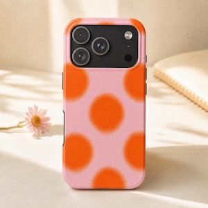 May include: A rectangular smartphone case featuring a light pink background with a repeating pattern of soft-edged, vibrant orange circular spots. The top section includes a black camera cutout area with three circular lens openings and a flash.
