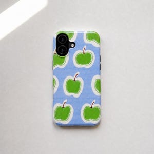 Könnte beinhalten: Eine rechteckige Smartphone-Hülle mit hellblauem Hintergrund, der mit mehreren grünen Äpfeln bedruckt ist. Jeder Apfel ist weiß umrandet und hat einen kleinen braunen Stiel. Die Hülle verfügt über eine Aussparung für eine Dual-Kamera.