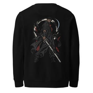 Pode incluir: Uma camisola preta de manga comprida com uma impressão gráfica nas costas. O design retrata uma personagem de estilo anime vestida com roupa escura, segurando uma espada comprida, contra um fundo circular abstrato em branco e vermelho.