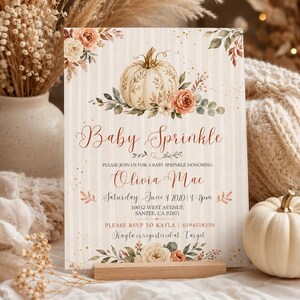 May include: A rectangular invitation card featuring a cream-colored striped background with a central illustration of a white pumpkin surrounded by orange and cream flowers and green leaves. The text reads Baby Sprinkle, Olivia Mae, Saturday June 4 2020, 10032 West Avenue, Santee, CA 92071, RSVP to Kayla 6194518350.