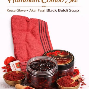 May include: A Moroccan Hammam Combo Set featuring a red textured Kessa glove, a clear jar of dark Akar Fassi Black Beldi Soap, and two small brass bowls filled with red powder, each containing a small wooden scoop, surrounded by red petals.