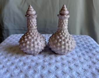 Puede incluir: Un par de saleros de cristal rosa pálido con una textura de puntos en relieve en los cuerpos redondeados y cuellos estrechos. Cada salero está rematado con un tapón puntiagudo y decorado con un fino borde dorado en el cuello y la base.