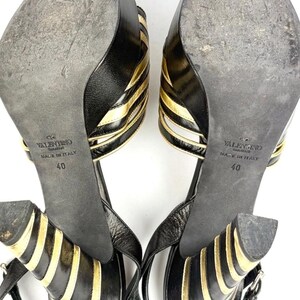 May include: Pair of black and gold Valentino high-heeled sandals. The sandals feature a strappy design with gold accents and a buckle closure. The soles are black and show wear, with the size 40 visible.