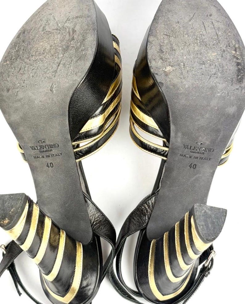 May include: Pair of black and gold Valentino high-heeled sandals. The sandals feature a strappy design with gold accents and a buckle closure. The soles are black and show wear, with the size 40 visible.