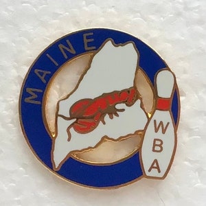 May include: A blue and gold enamel pin featuring a white outline of the state of Maine, a red lobster, and a bowling pin with the letters WBA. The pin is a souvenir from Maine.