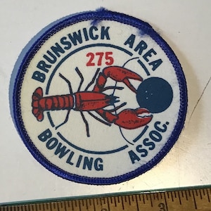 May include: A blue and white embroidered patch with a red lobster holding a blue bowling ball. The text on the patch reads "Brunswick Area Bowling Assoc. 275".