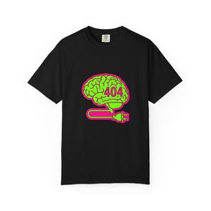 May include: Black t-shirt featuring a neon green brain graphic with the number "404" and a pink plug. The brain graphic is connected to a pink plug. The t-shirt is a classic crew neck style.