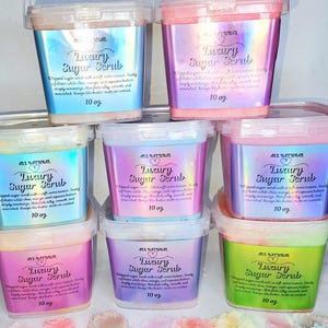 May include: An assortment of colorful, square containers of "Luxury Sugar Scrub" with silver handles. Each container has a holographic label and contains 10 oz of product. The image also shows a colorful pile of sugar scrub.