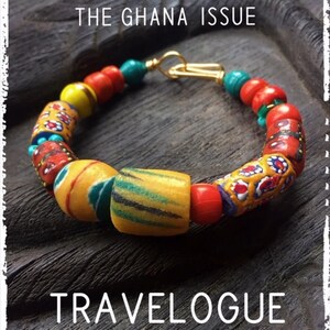 Op de afbeelding: Een close-up van een kleurrijke kralenarmband met een gouden sluiting. De kralen zijn rood, geel, blauw en groen. De armband ligt op een donker houten oppervlak. De tekst "Winter 2021 THE GHANA ISSUE TRAVELOGUE MAGAZINE" is zichtbaar in de afbeelding.
