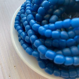 May include: A close-up of a pile of blue glass beads. The beads are round and have a smooth, polished finish.