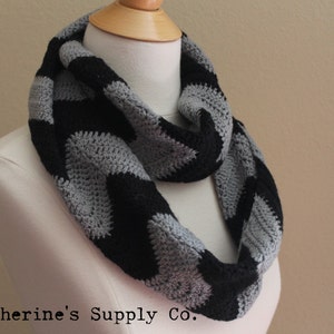 Könnte beinhalten: Ein grauer und schwarzer gehäkelter Infinity-Schal mit Chevron-Muster.